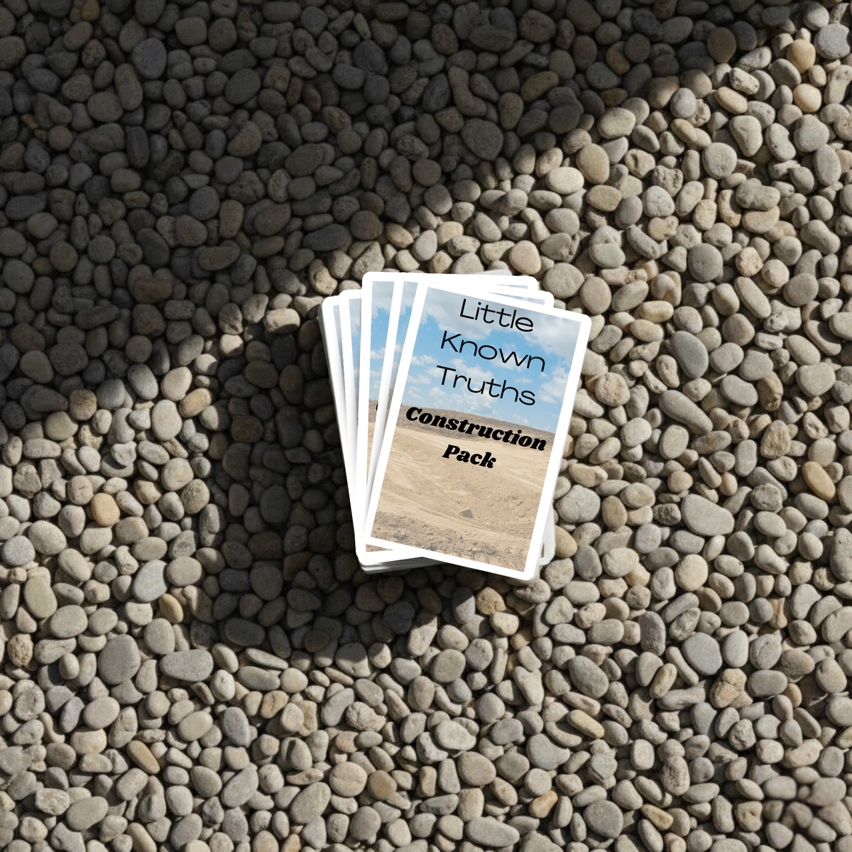 Card pack titled 'Little Known Truths Construction Pack' on pebbles